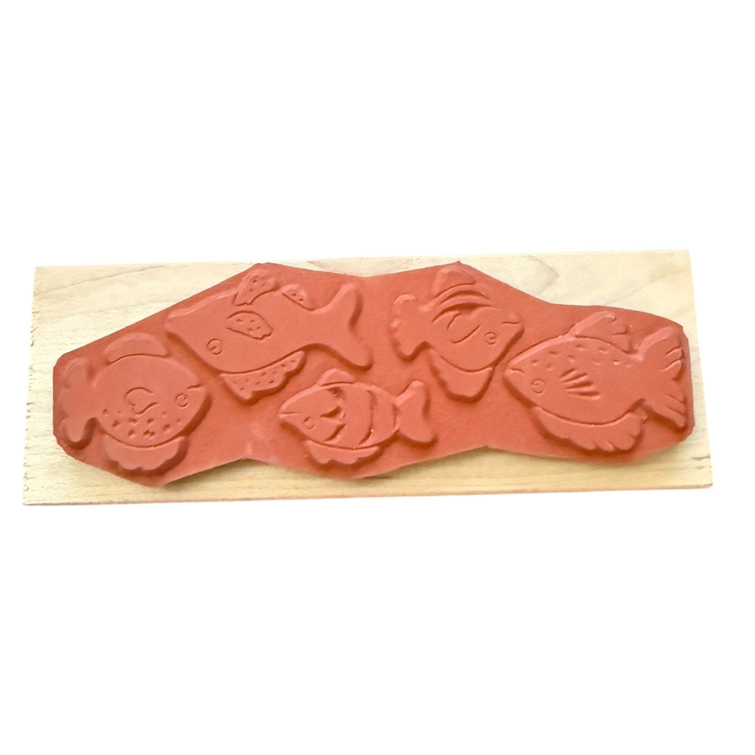A terracotta-colored rubber stamp featuring embossed fish designs, mounted on a rectangular light wood block against a plain white background.