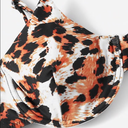 Close-up of a bikini top with a bold leopard print pattern in orange, black, and white, shown against a plain light background.