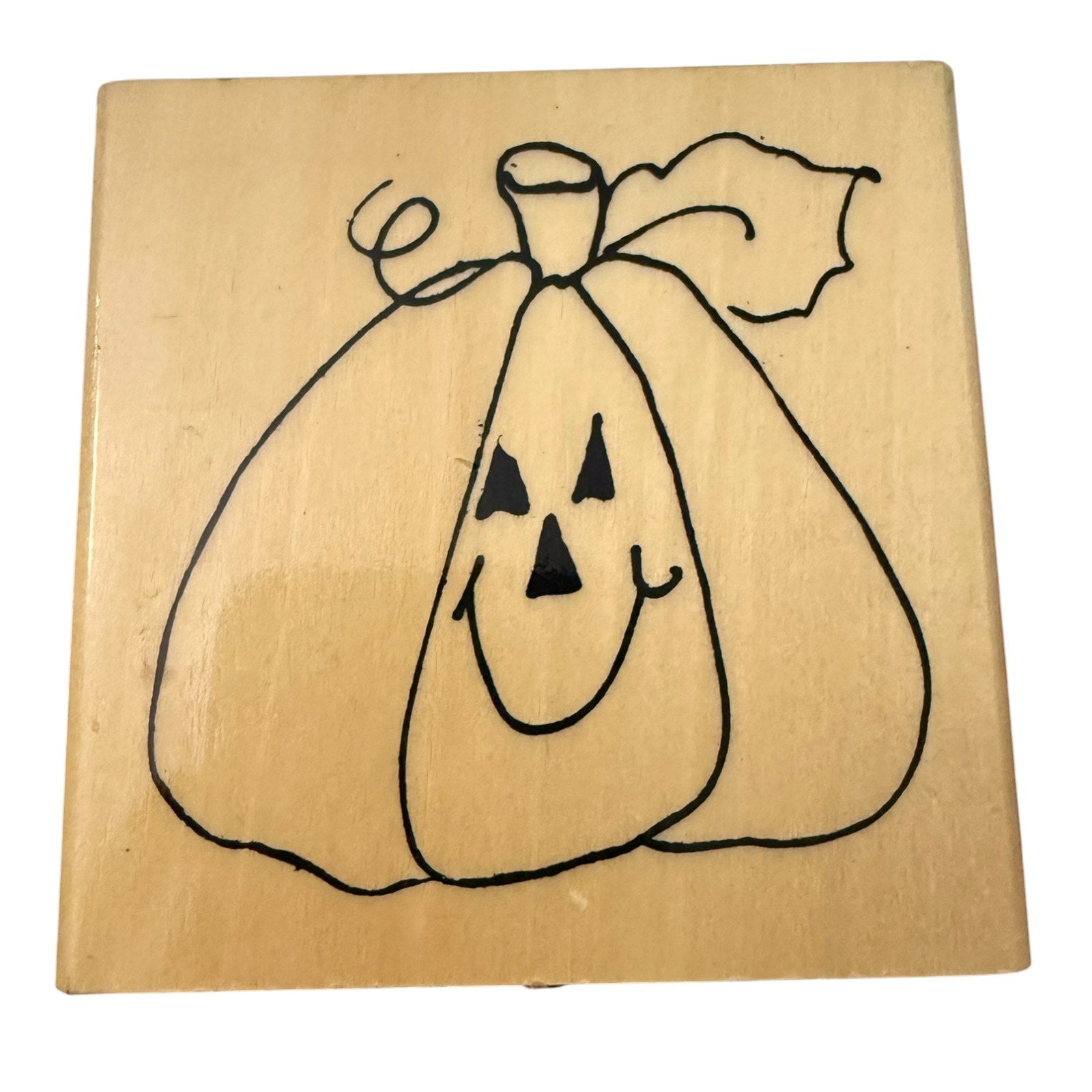 A square wooden stamp block featuring a black line-art pumpkin face with triangular eyes and mouth, photographed on a plain white background.