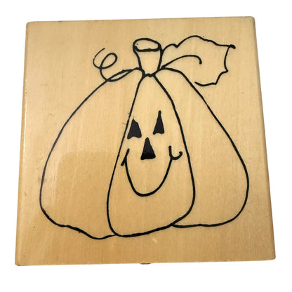 A square wooden stamp block featuring a black line-art pumpkin face with triangular eyes and mouth, photographed on a plain white background.