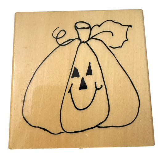 A square wooden stamp block featuring a black line-art pumpkin face with triangular eyes and mouth, photographed on a plain white background.