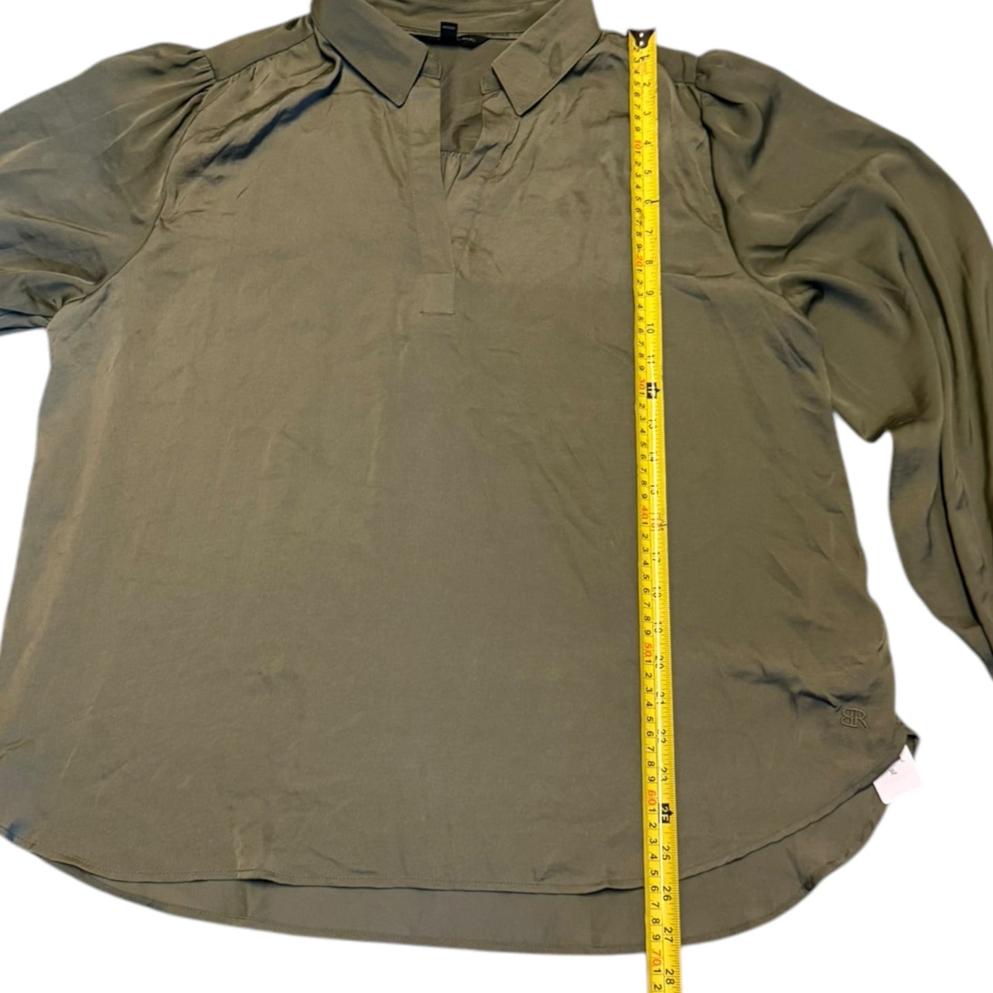 An olive green long-sleeve shirt laid flat on a white background, with a yellow measuring tape vertically placed to show its height.