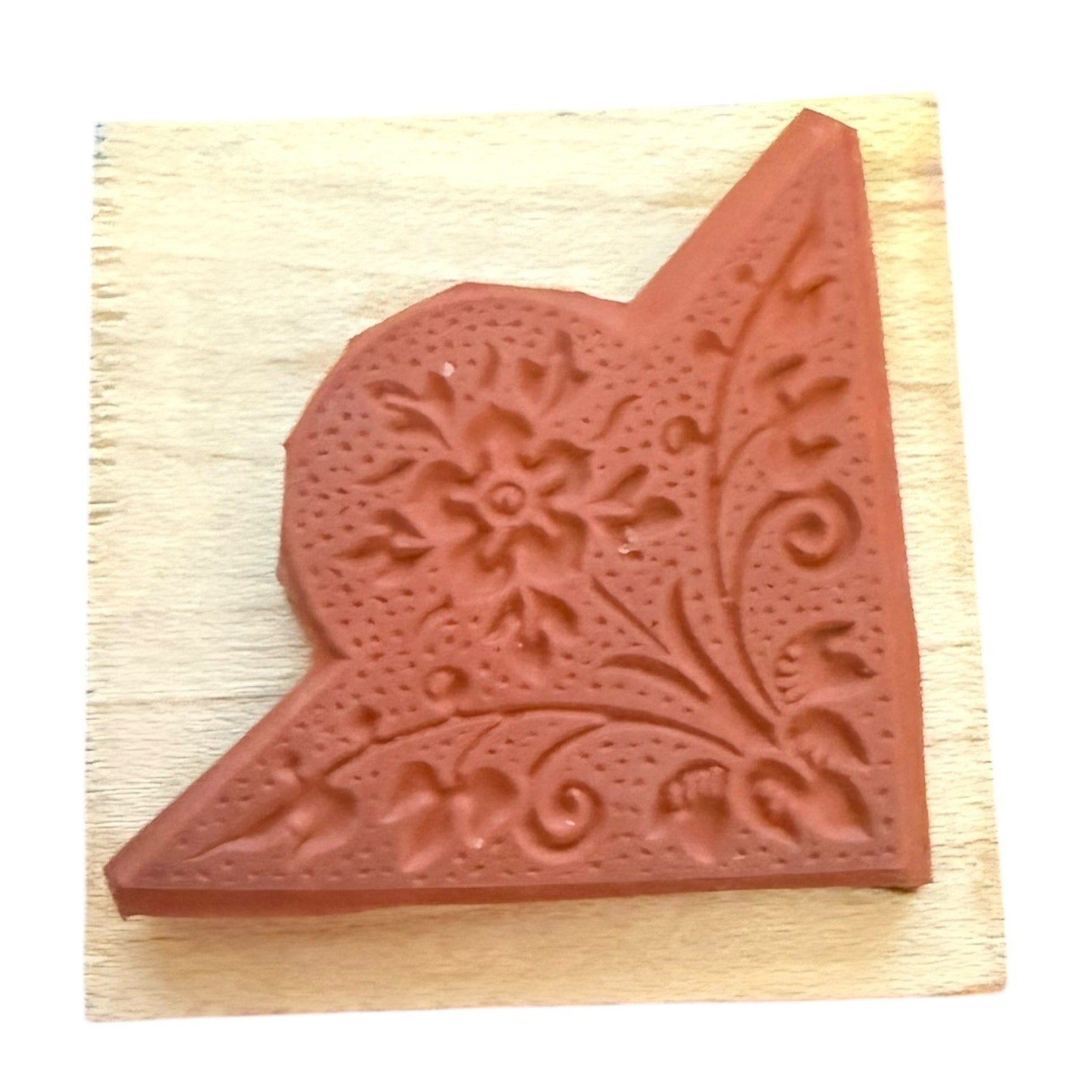 Decorative terracotta colored stamp with floral design on a wooden block
