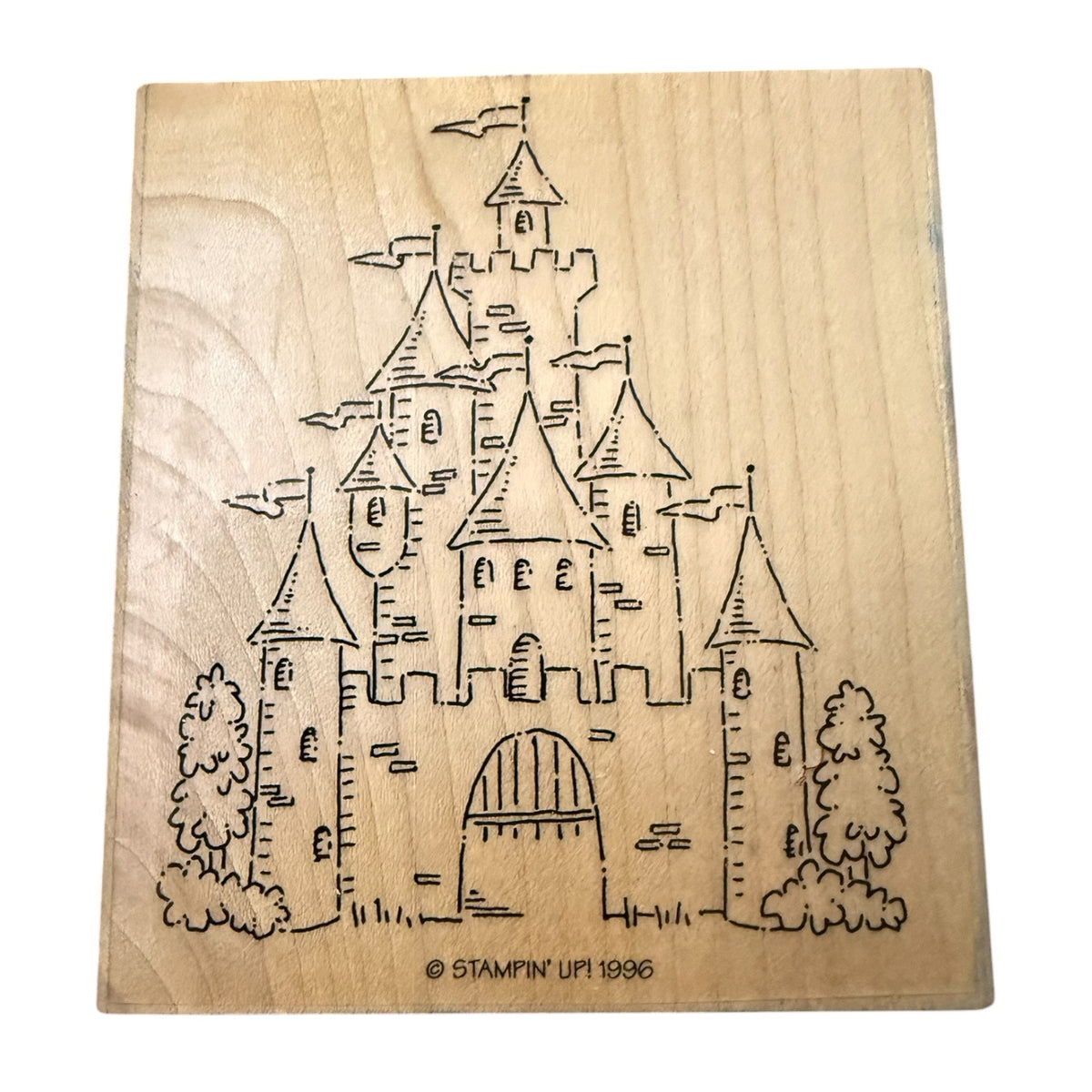 A square natural wood stamp block featuring a drawing of a castle with towers, flags, trees, and an arched gate. Small text at the bottom reads “© STAMPIN' UP! 1996.