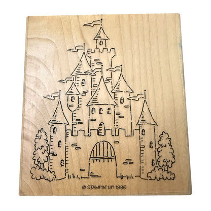 A square natural wood stamp block featuring a drawing of a castle with towers, flags, trees, and an arched gate. Small text at the bottom reads “© STAMPIN' UP! 1996.