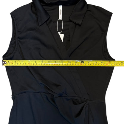 A black sleeveless collared wrap-style dress laid flat on a white background, with a yellow tape measure stretched horizontally across the chest to show the width.