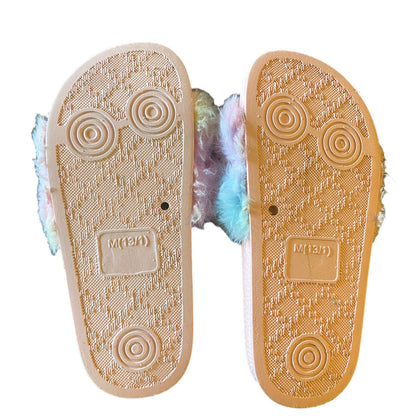 A pair of plush slippers shown from the sole side, featuring a textured pink rubber outsole with circular tread patterns and a fluffy pastel rainbow lining peeking out from the sides.