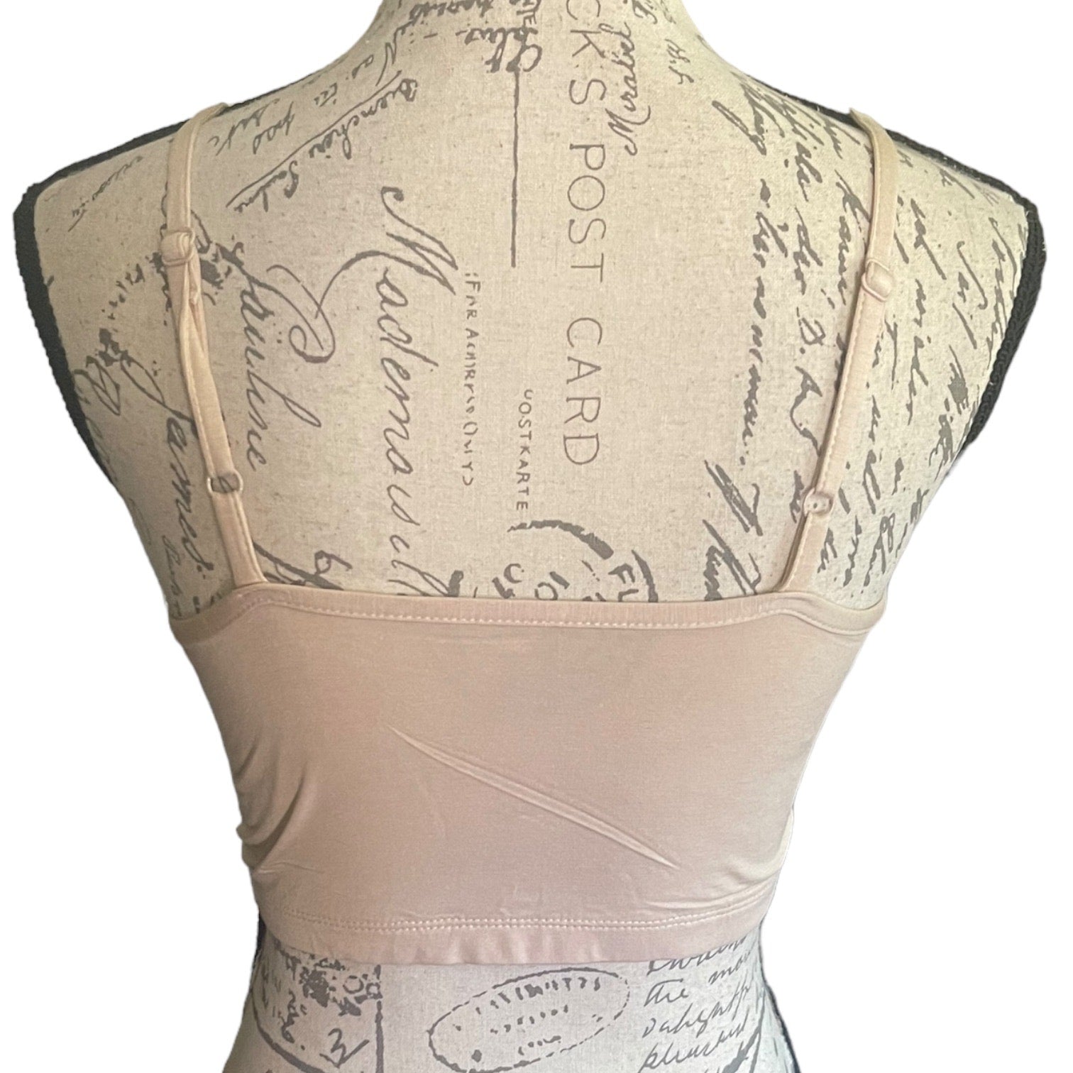 A beige bralette displayed on a vintage-style dress form mannequin, showing the back view with adjustable shoulder straps and a wide waistband.