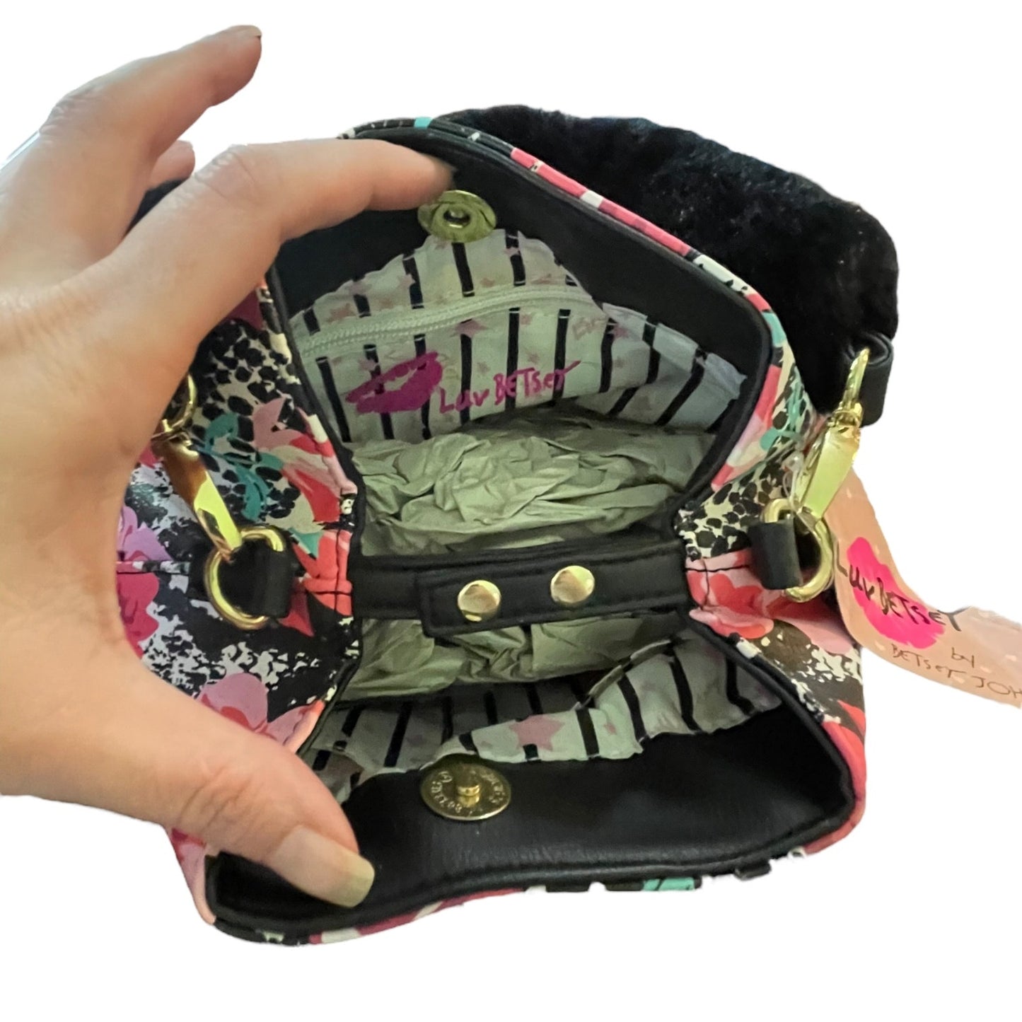 A hand holding open a small floral and black-and-white patterned bag with a black faux-fur trim, hardware.