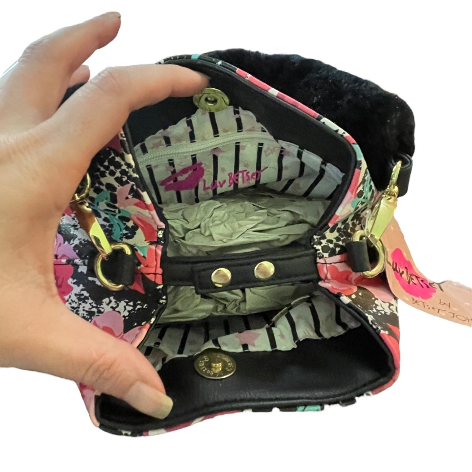 A hand holding open a small floral and black-and-white patterned bag with a black faux-fur trim, hardware.