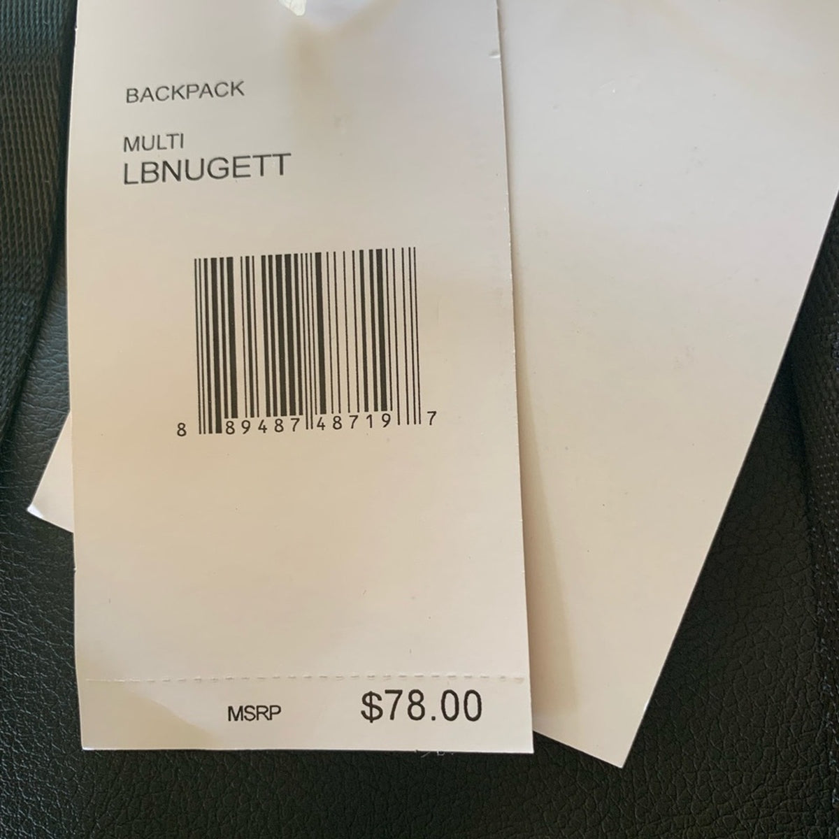 A close-up of a white paper price tag attached to a backpack, showing the text 'BACKPACK MULTI LBNUGETT' and a barcode. The tag also shows an MSRP price of $78.