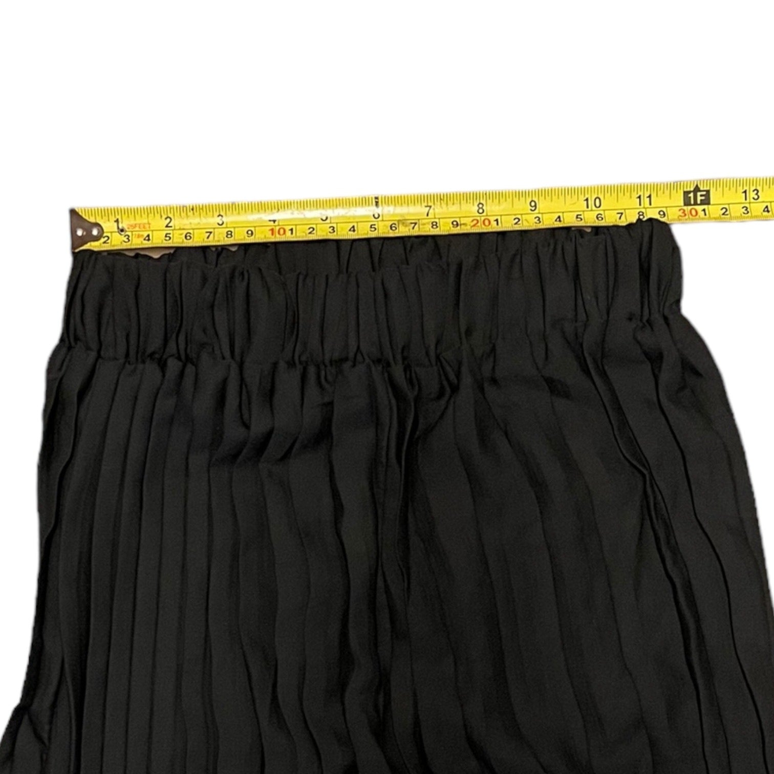 Black pleated pants with a gathered elastic waistband, shown with a yellow tape measure across the top to indicate size.