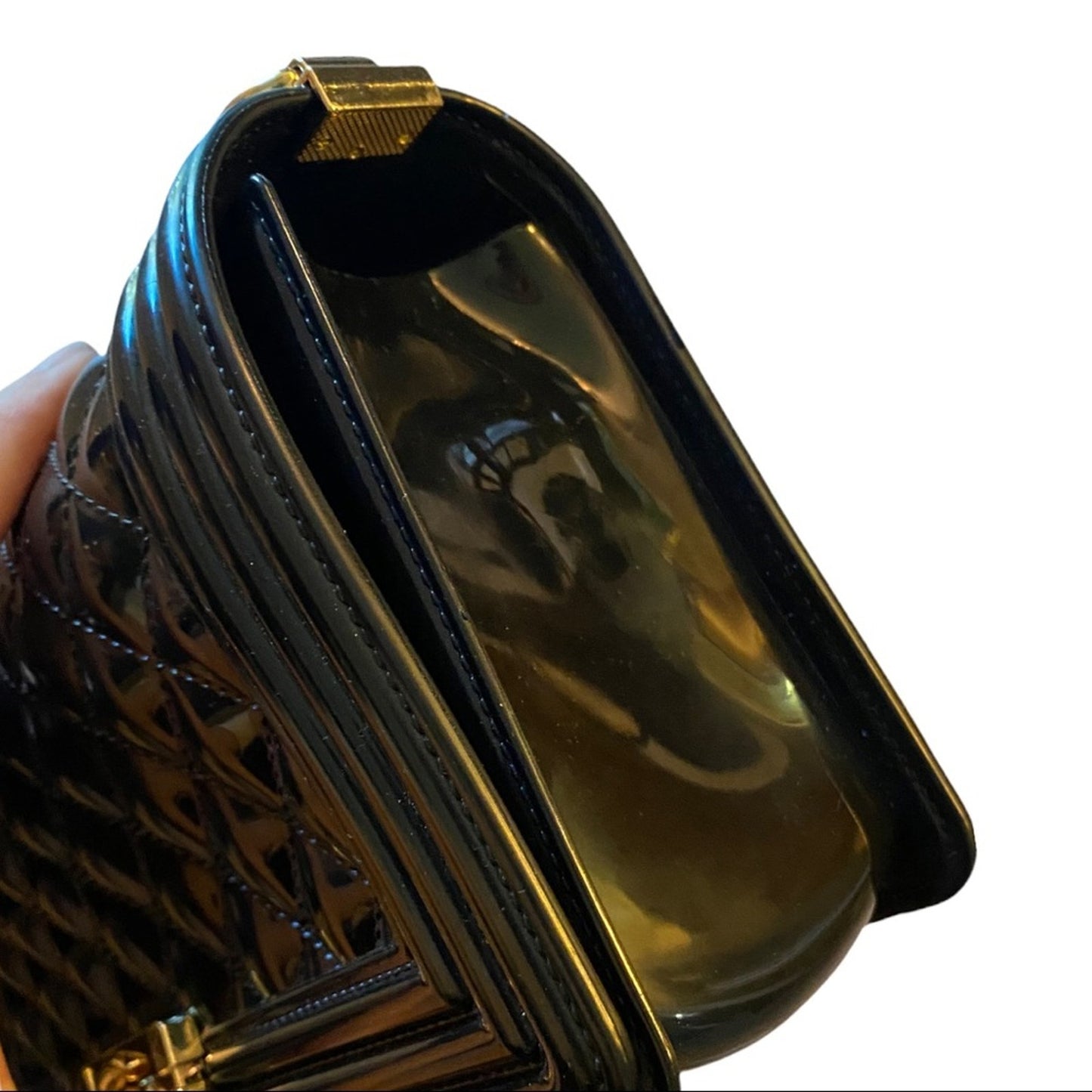Side view of black purse with gold accents held by a hand on a white background