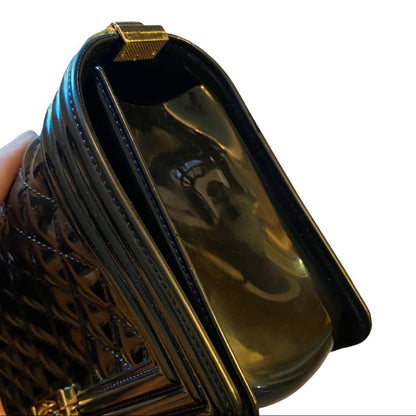 Side view of black purse with gold accents held by a hand on a white background