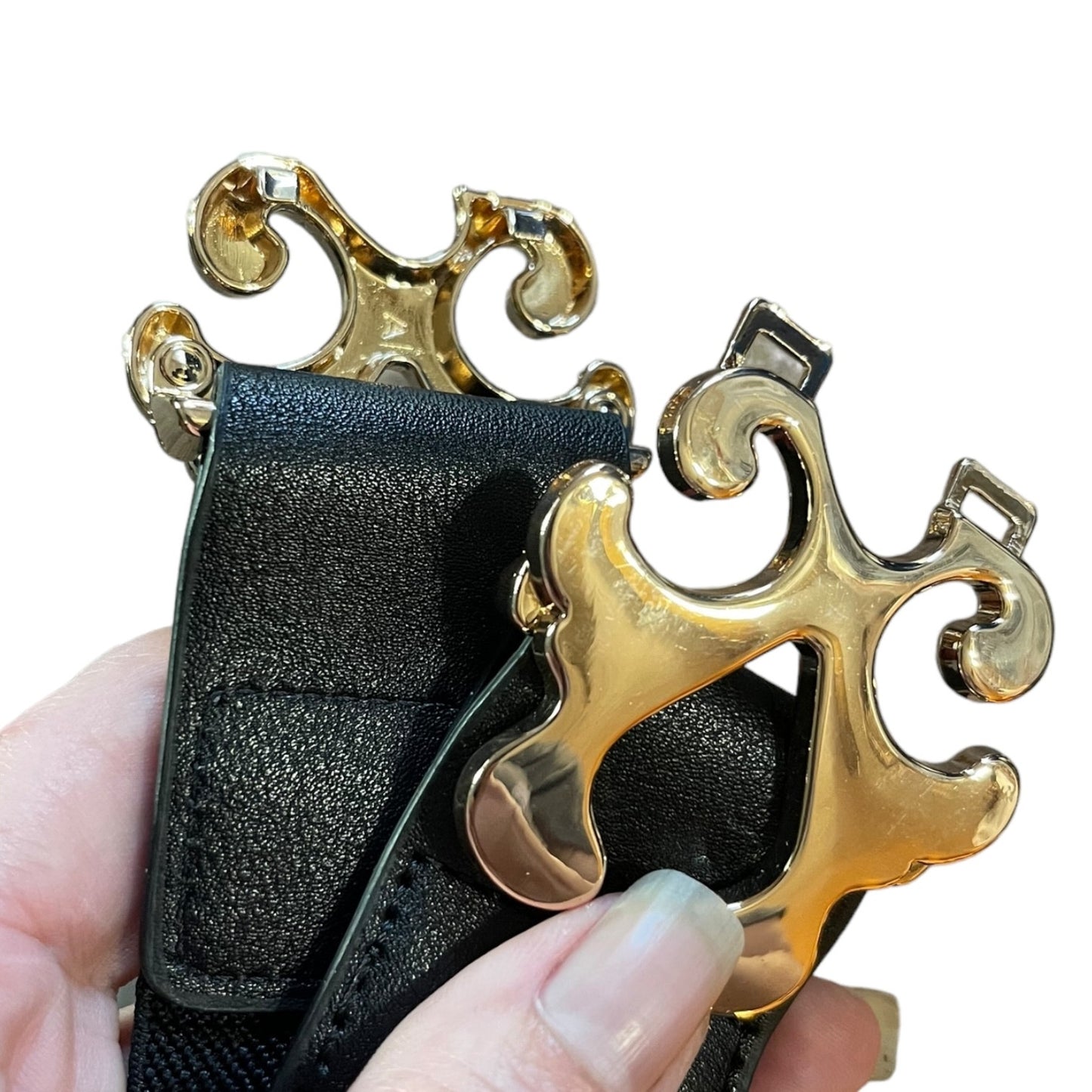 A close-up of a hand holding a black textured belt with a large, ornate gold-tone metal buckle.
