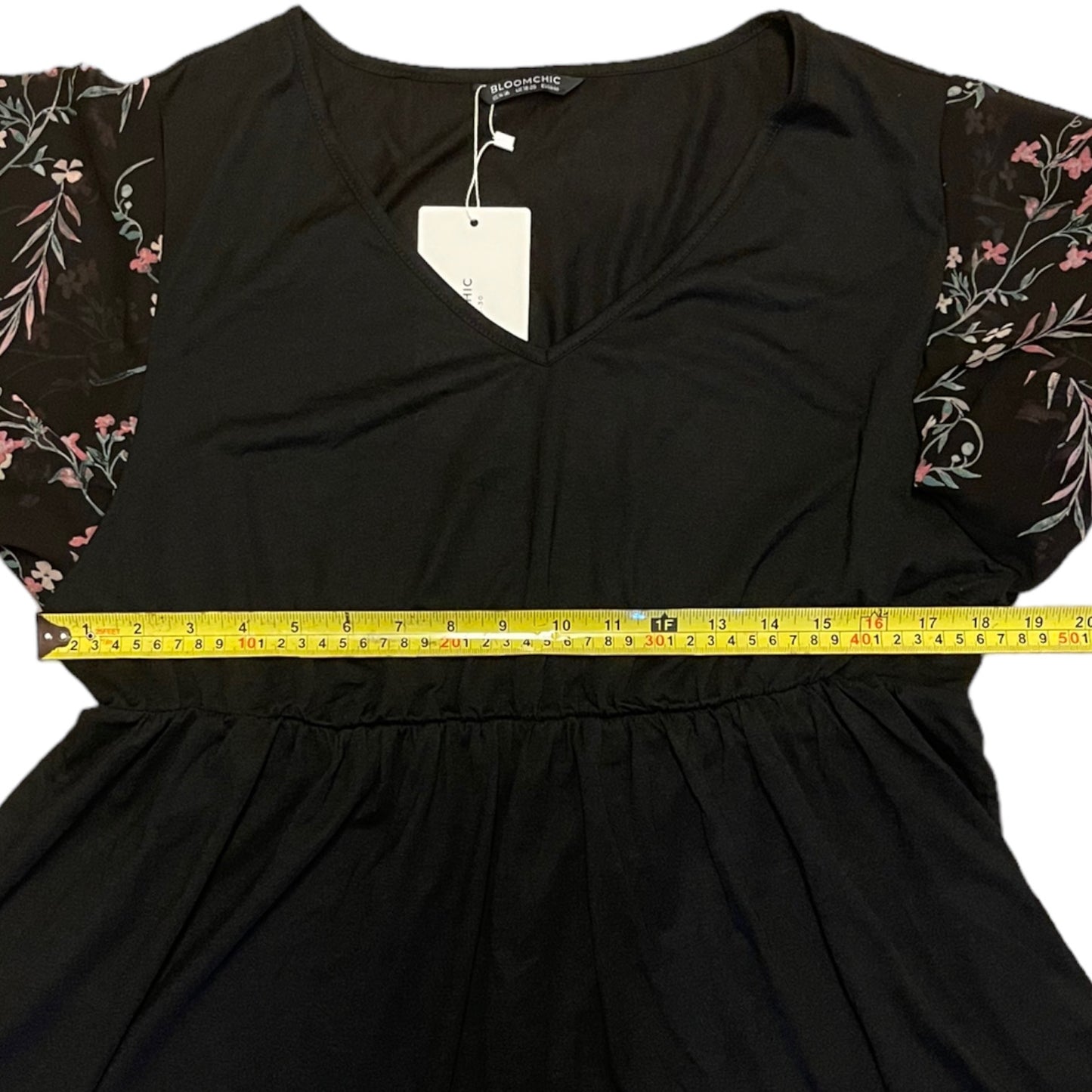 Black shirt with floral sleeves being measured with a tape measure on a white background