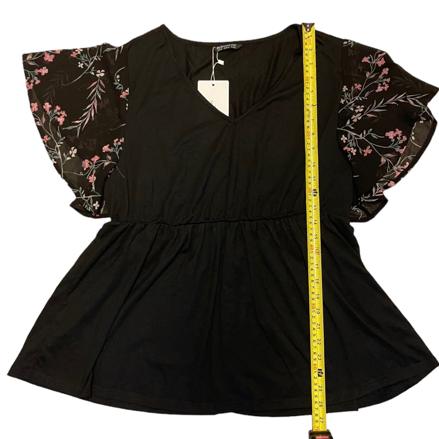 Black shirt with floral sleeves and a measuring tape for size reference on a white background