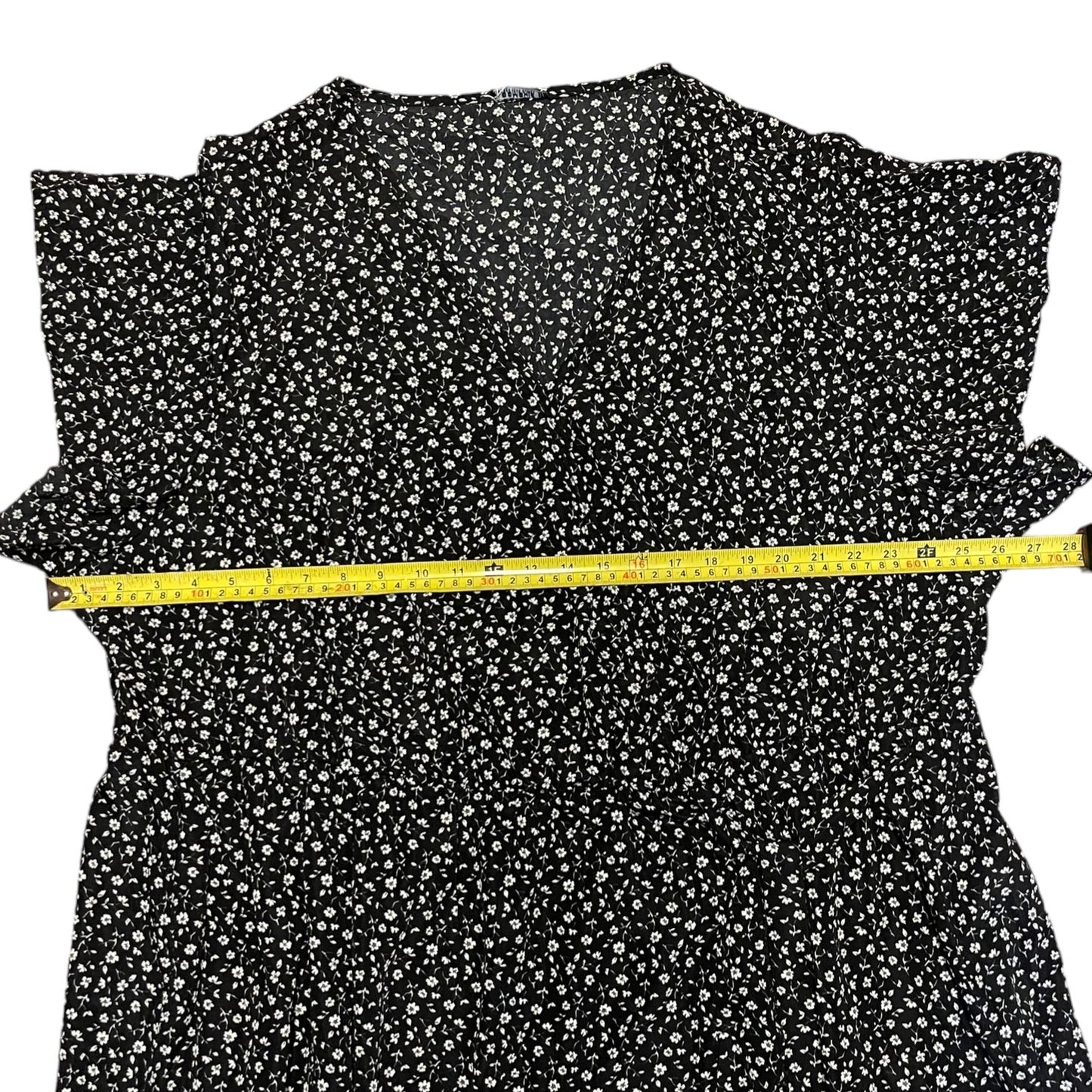 Black dress with white floral pattern and a measuring tape on a white background