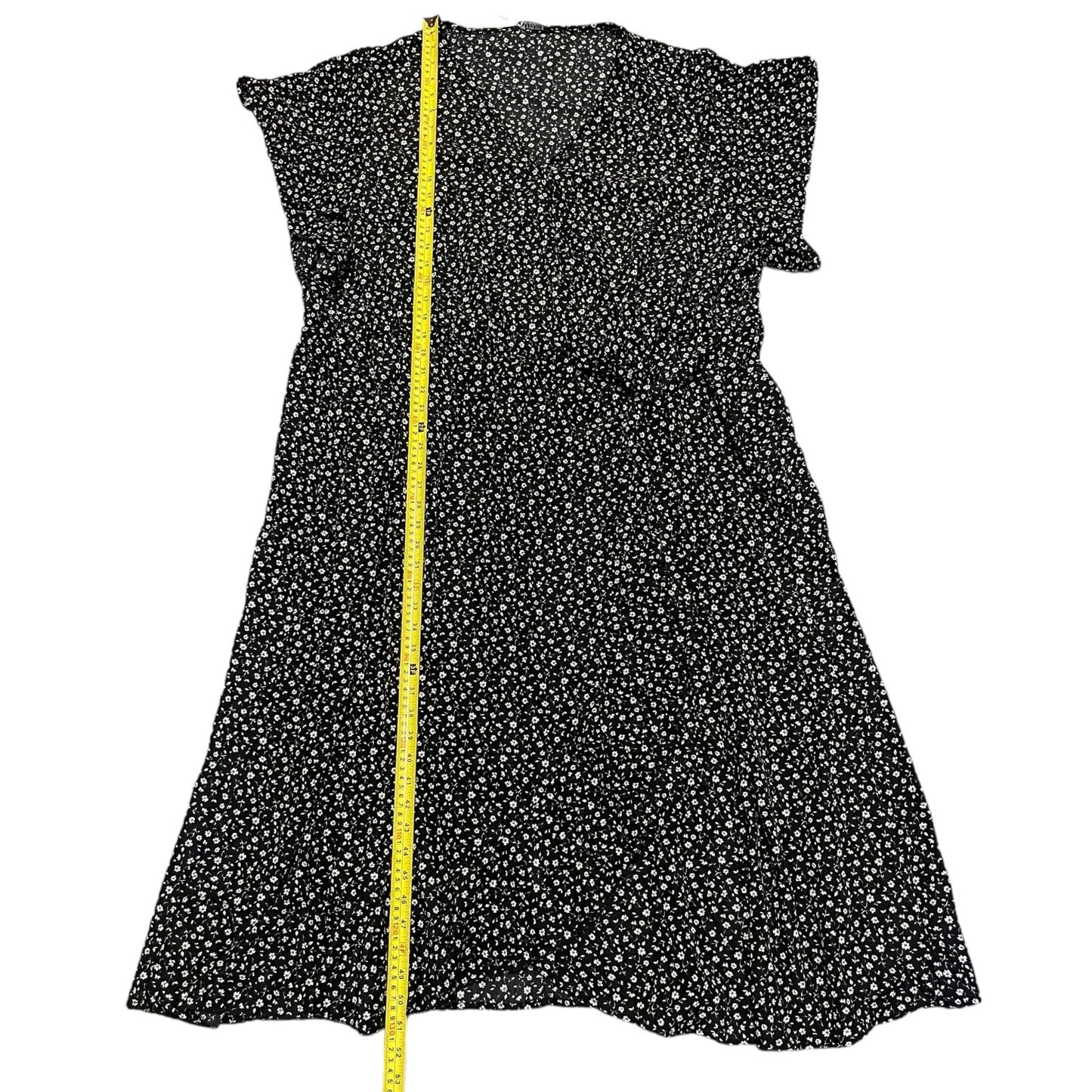 Black dress with white floral pattern and a yellow measuring tape on a white background