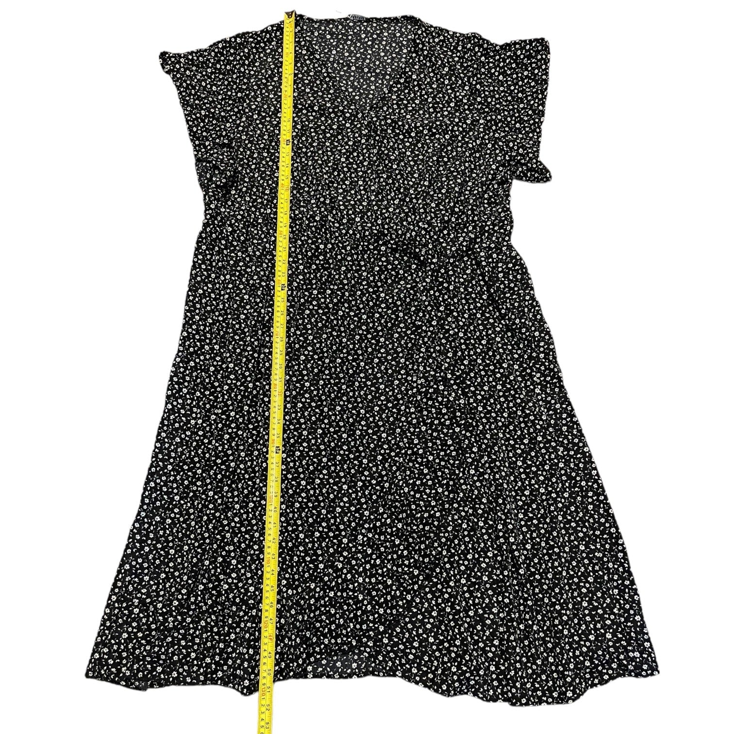 Black dress with white floral pattern and a yellow measuring tape on a white background