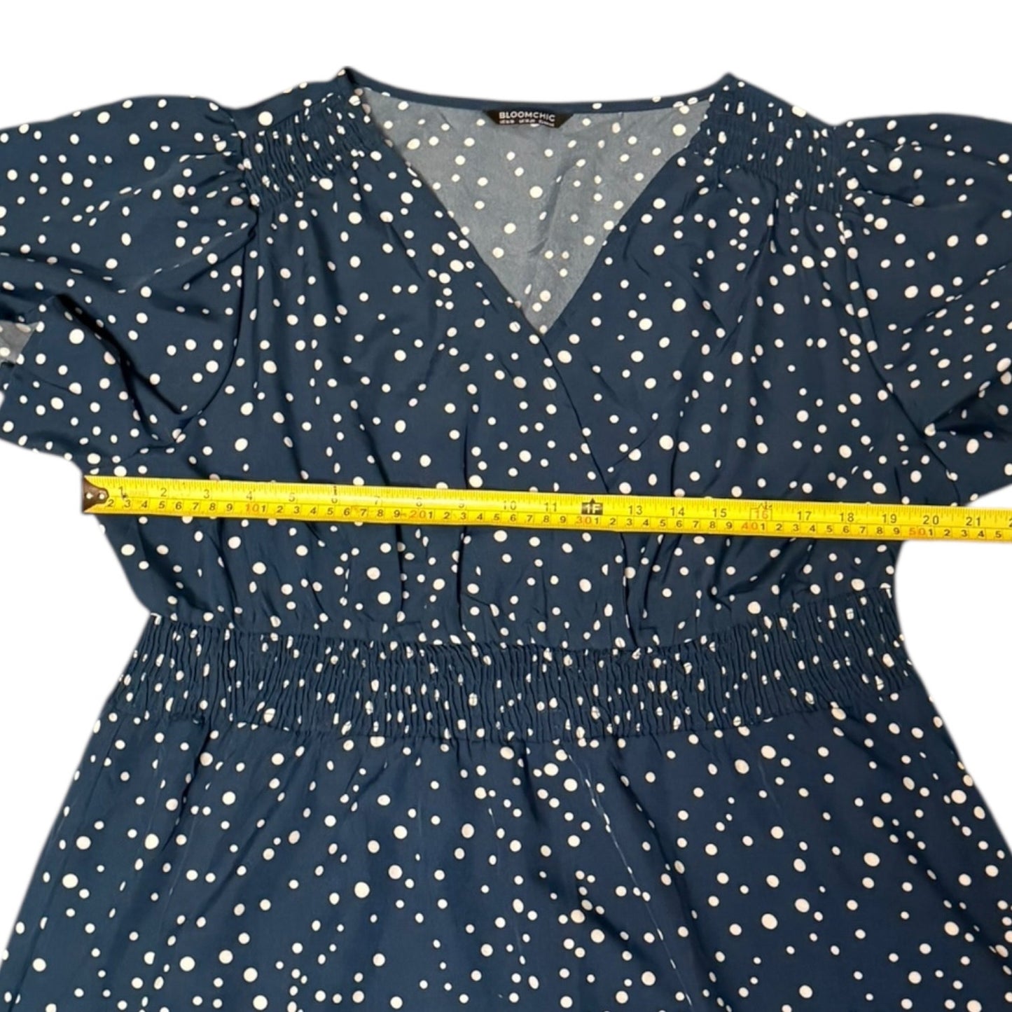 Navy dress with white polka dots and a yellow measuring tape around the waist on a white background