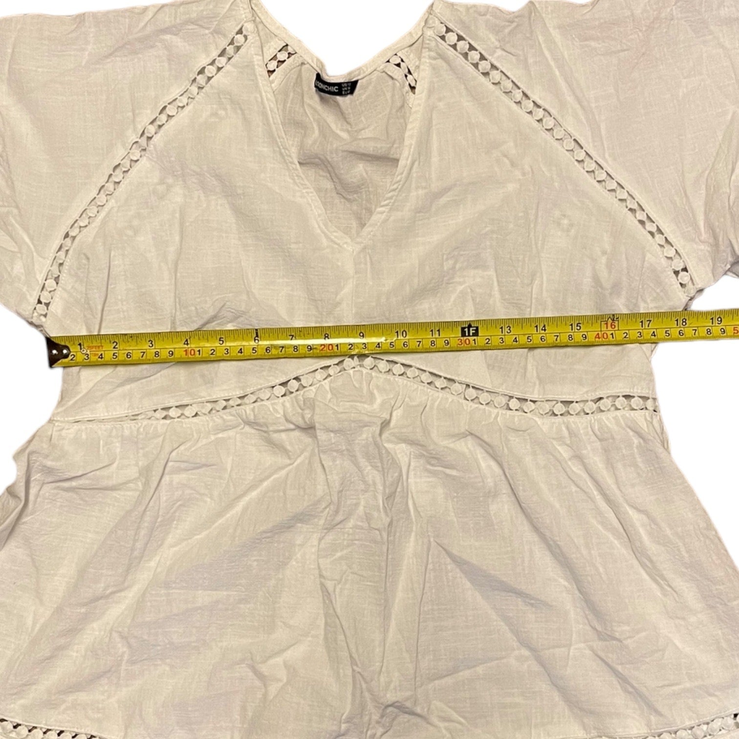white top with decorative trim and a measuring tape laid across it on a white background