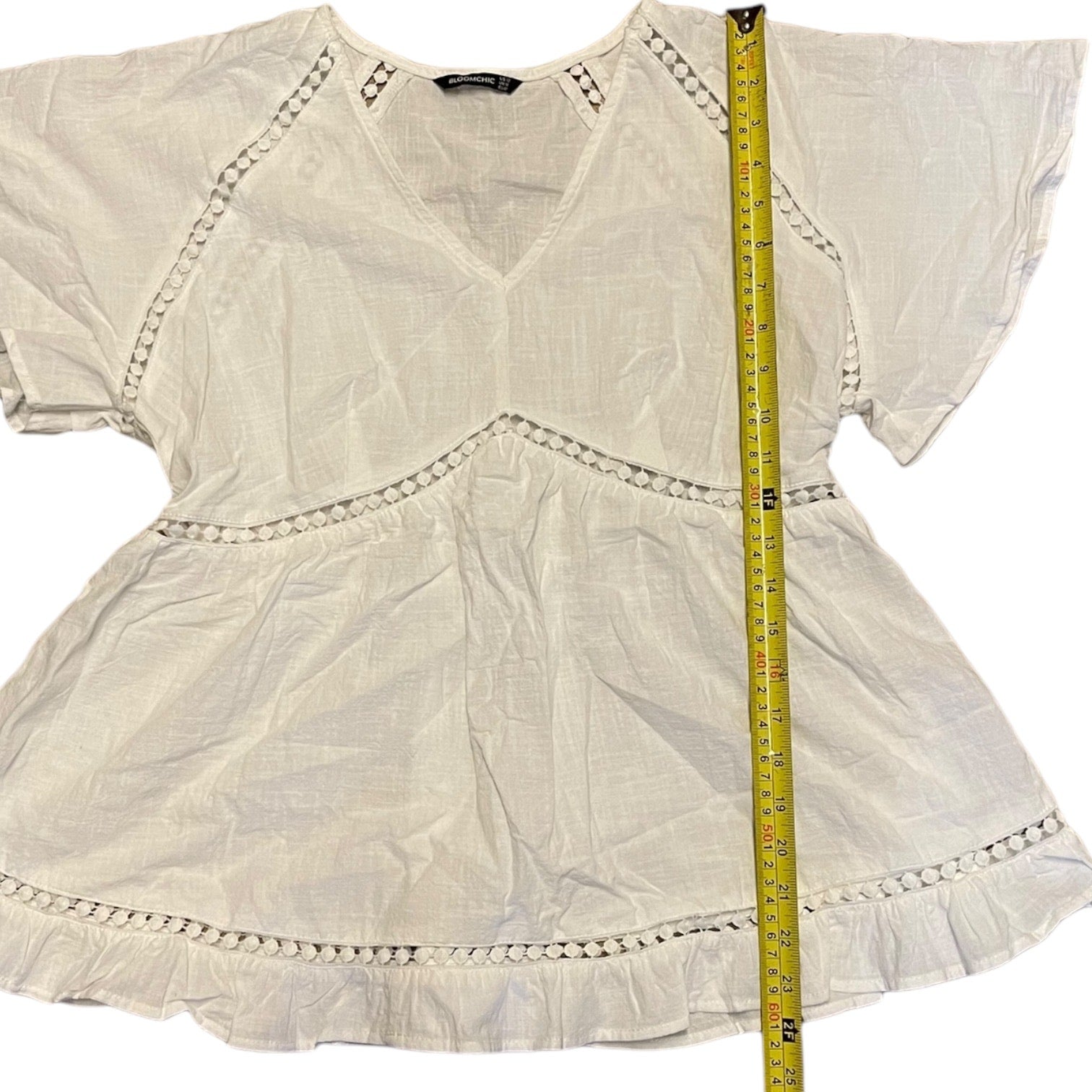 White blouse with decorative trim and a measuring tape for size reference on a white background