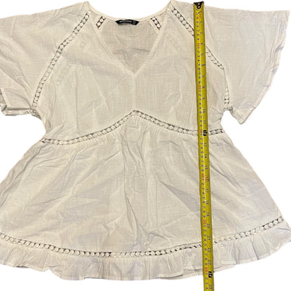White blouse with decorative trim and a measuring tape for size reference on a white background