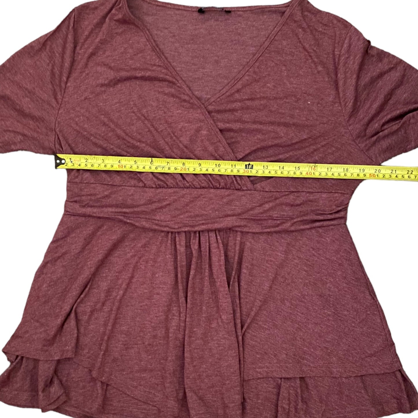 A heathered dusty rose wrap-style top with short sleeves and a tiered ruffled hem, shown flat on a white background with a yellow tape measure across the waist area to indicate size.