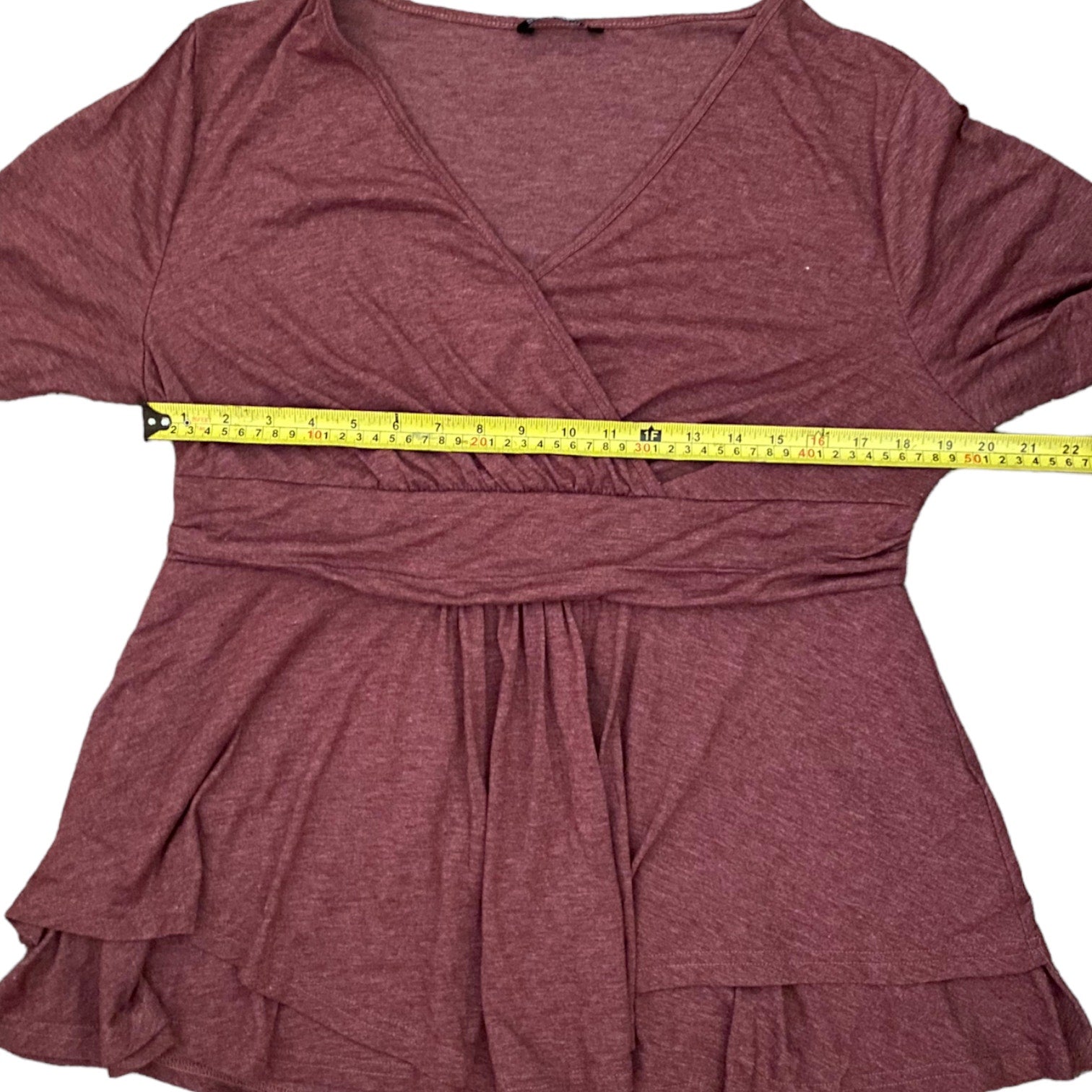 A heathered dusty rose wrap-style top with short sleeves and a tiered ruffled hem, shown flat on a white background with a yellow tape measure across the waist area to indicate size.
