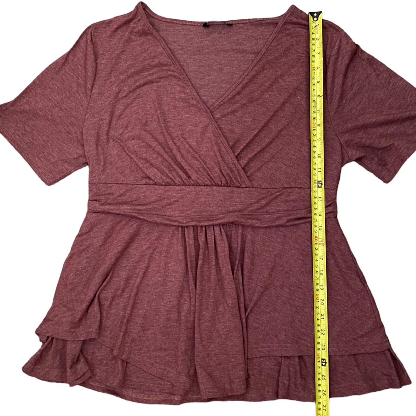 A heathered dusty rose wrap-style short-sleeve top with a ruffled tiered hem, shown flat on a white background with a yellow measuring tape standing vertically to indicate the garment's height.