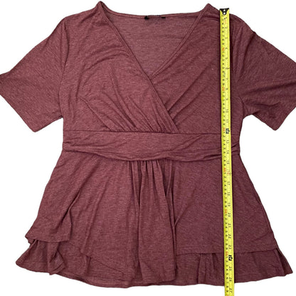 A heathered dusty rose wrap-style short-sleeve top with a ruffled tiered hem, shown flat on a white background with a yellow measuring tape standing vertically to indicate the garment's height.