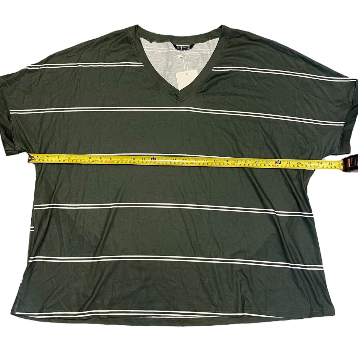 An dark green V-neck t-shirt with thin white horizontal stripes, shown flat-laid with a yellow measuring tape stretched across the chest to indicate width.