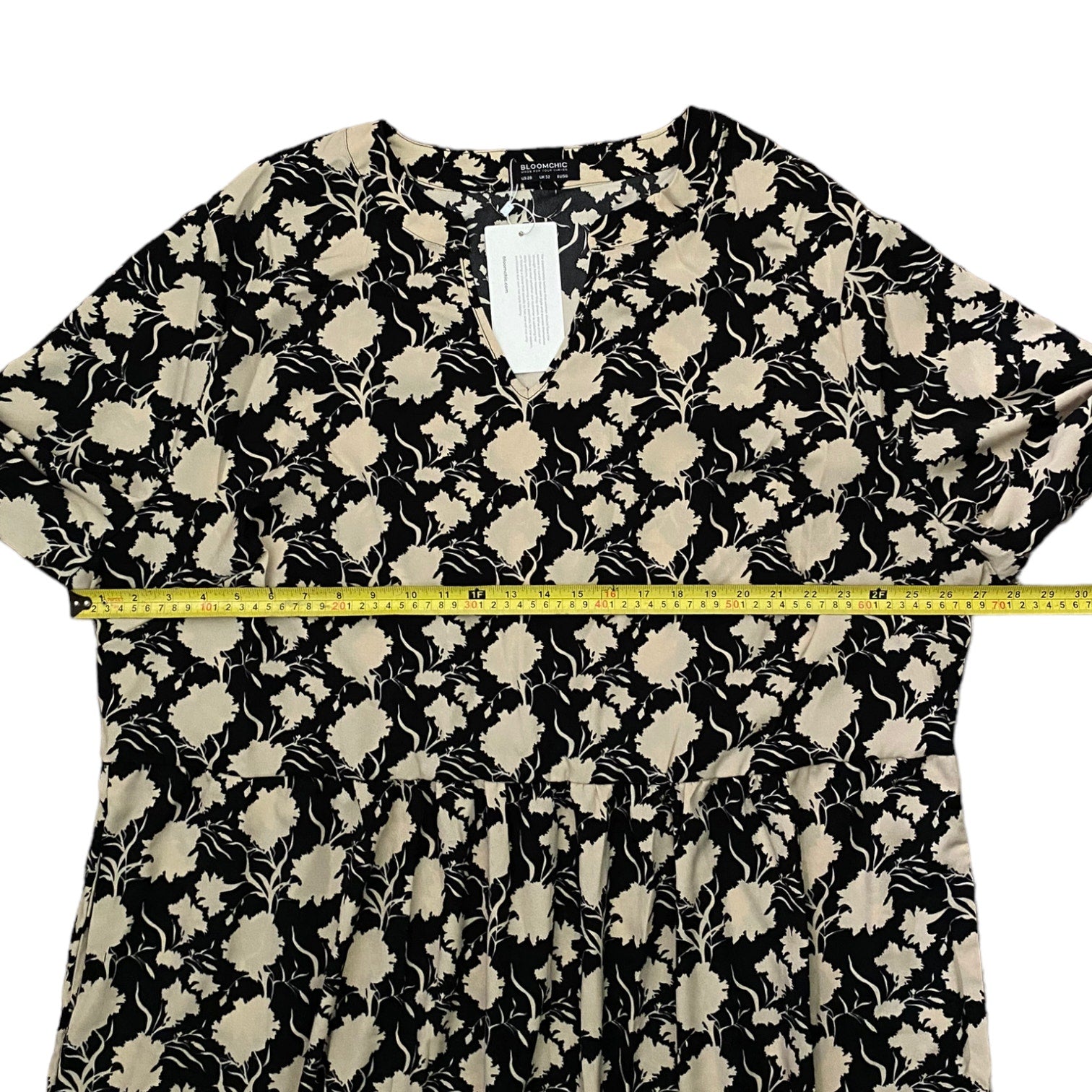 A black and beige floral print dress laid flat on a white background, with a yellow measuring tape stretched horizontally across the waist area to show the width.
