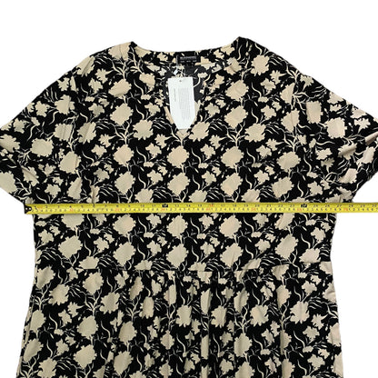 A black and beige floral print dress laid flat on a white background, with a yellow measuring tape stretched horizontally across the waist area to show the width.