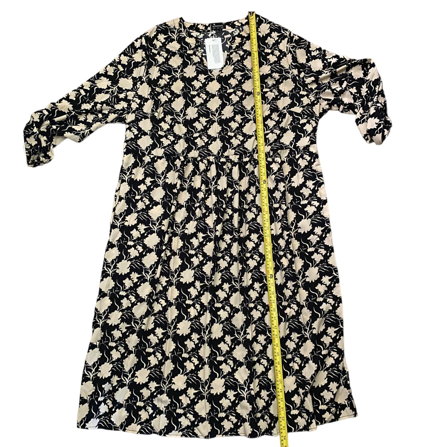 A black and beige floral print dress , shown flat on a white background with a yellow measuring tape running down the center to indicate size.
