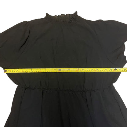 A black dress laid flat on a white background with a yellow tape measure stretched horizontally across the waist area to show the garment's measurements.