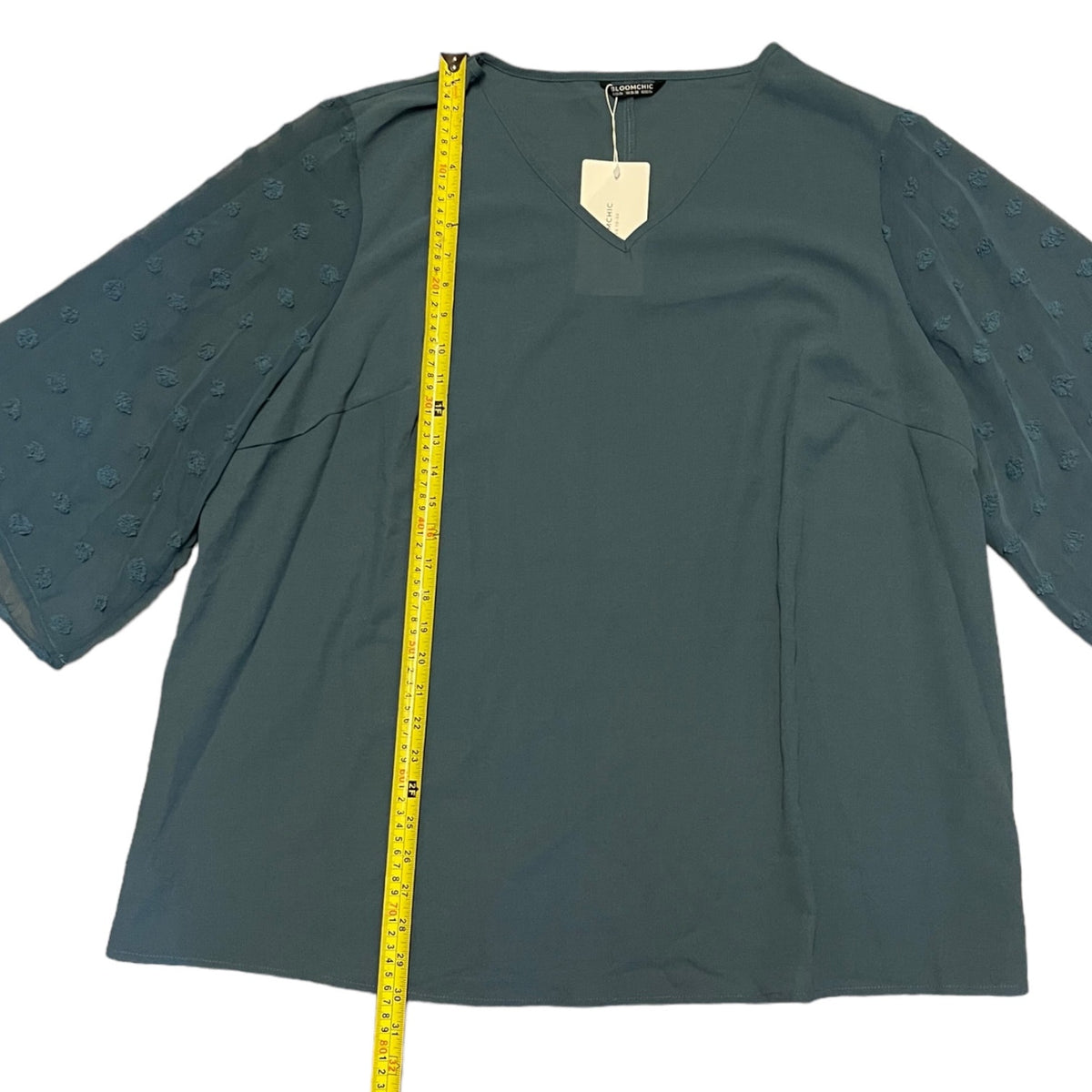  long-sleeve blouse with textured, raised dot patterns on the sleeves, shown flat with a yellow measuring tape vertically aligned on the left side for scale.