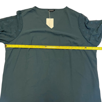 top with textured puff sleeves, shown flat with a yellow measuring tape stretched across the chest to indicate width. A blank paper tag is attached to the neckline.
