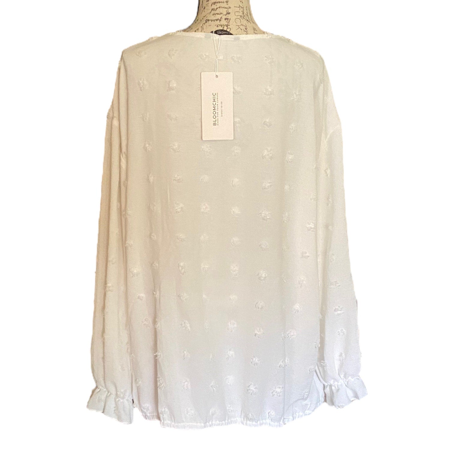 Back of white polka dot blouse on a mannequin with a visible tag against a white background