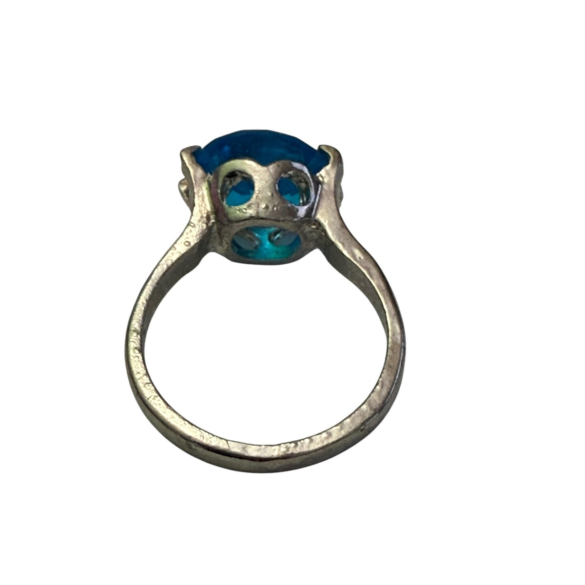 A silver ring featuring a unique shaped setting holding a vibrant blue oval stone , shown against a plain white background.