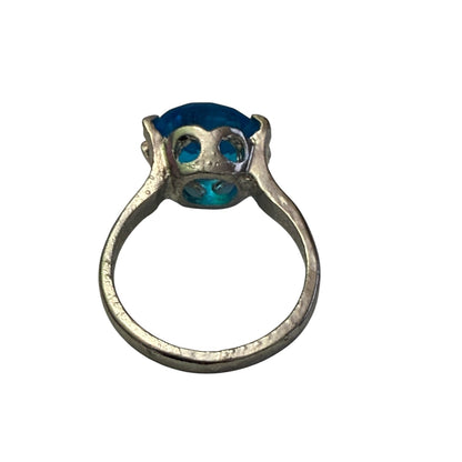 A silver ring featuring a unique shaped setting holding a vibrant blue oval stone , shown against a plain white background.