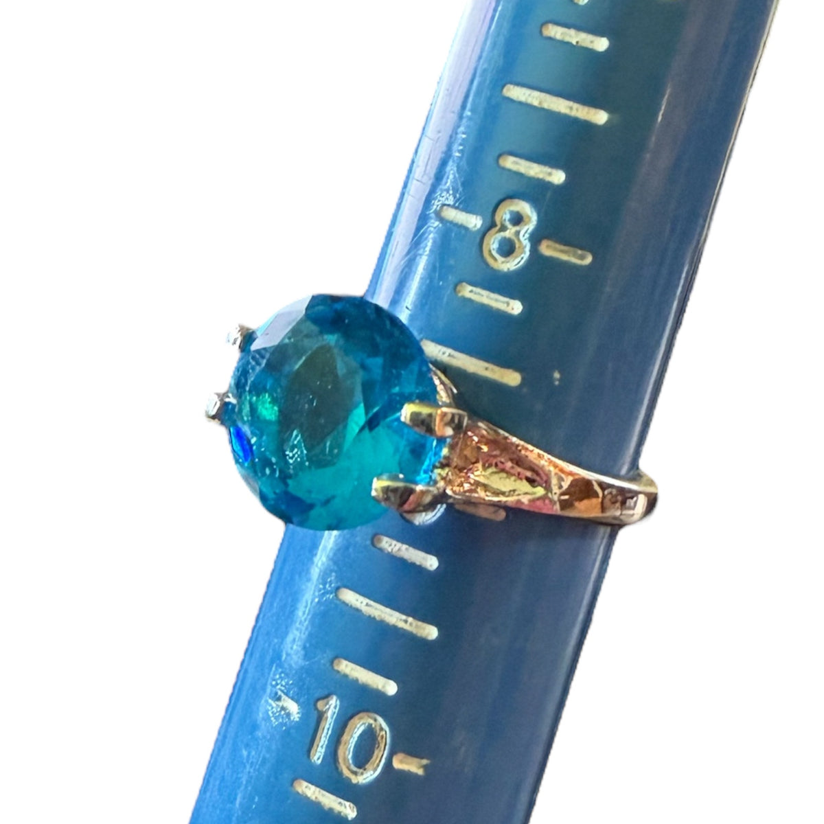 A round-cut blue stone ring with a silver-colored band, shown resting on a blue plastic ring sizer with markings.
