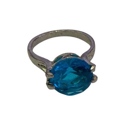 A silver-toned ring featuring a large, round-cut blue stone in a prong setting, shown against a plain white background.