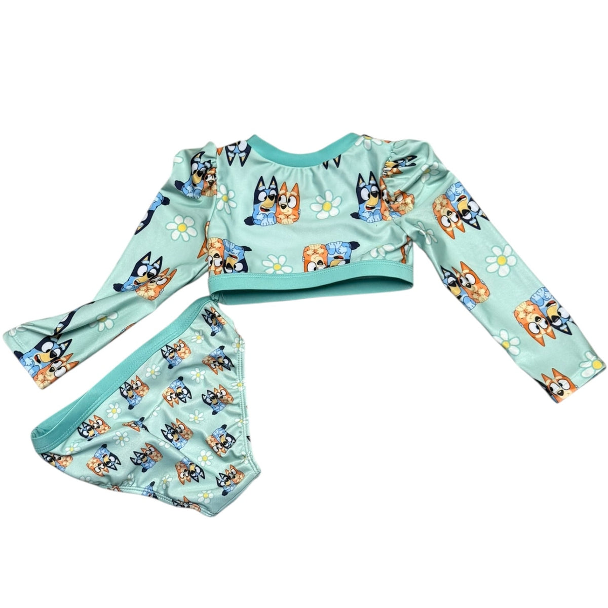 A two-piece children's swim set featuring a long-sleeve top and matching bottoms in a light mint green color, both printed with cartoon dogs and white daisies. 