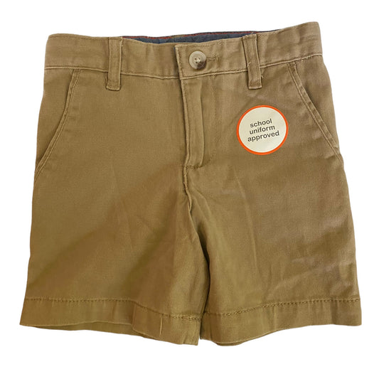 A pair of beige cotton chino shorts for boys with adjustable waistband, button/zip front, and two front and back pockets.