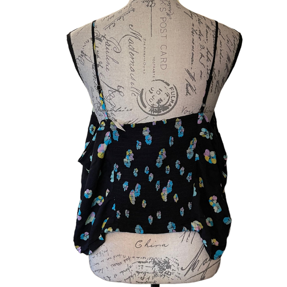 Black sleeveless top with thin shoulder straps and a multicolor floral print, displayed on a beige fabric mannequin torso against a white background.