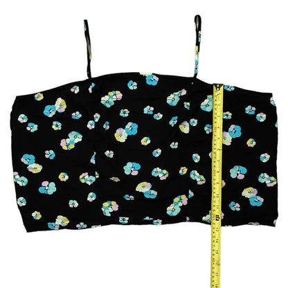 A black spaghetti-strap crop top with a colorful pastel floral pattern, shown flat with a yellow measuring tape standing vertically on the right side.