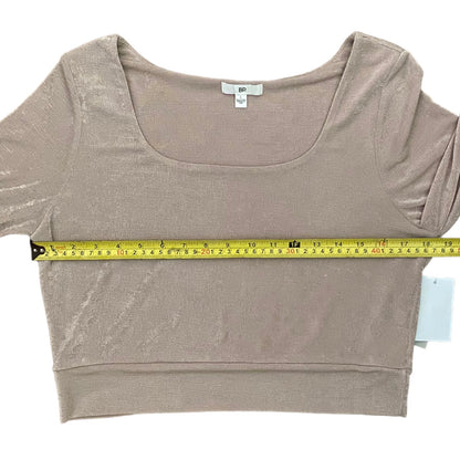 A light pink top laid flat on a white background, with a yellow tape measure stretched horizontally across the chest to show the width.