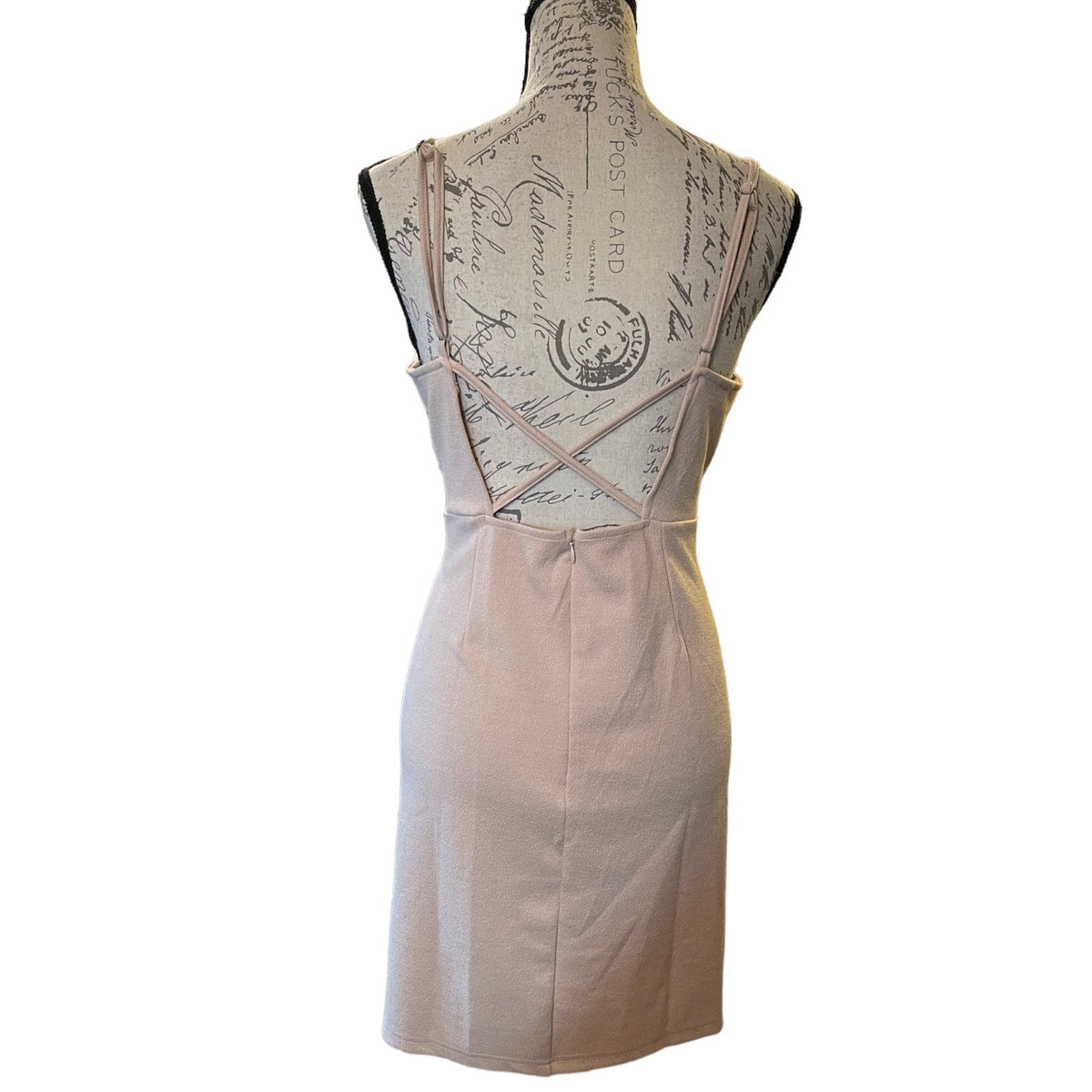 A sleeveless light beige  displayed on a vintage-style dress form mannequin, showing the back design with thin crisscross straps and a straight skirt, set against a plain white background.